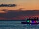 An ocean sunset with a boat with rainbow colored lighting